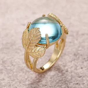 Primer plano detallado del anillo de hoja de ginkgo dorada con una piedra azul brillante.