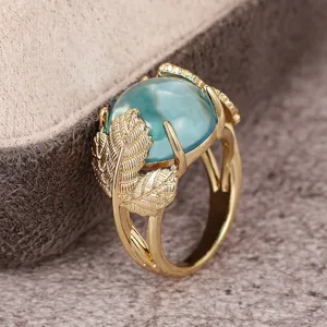 Detalle en primer plano de un anillo de mujer dorado con tallas de hojas y piedra azul.