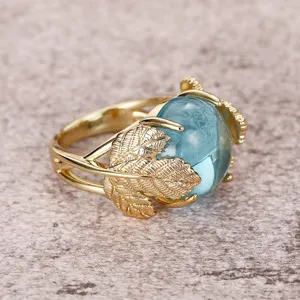 Anillo dorado elegante para mujer con piedra azul translúcida y diseño de hoja de ginkgo.