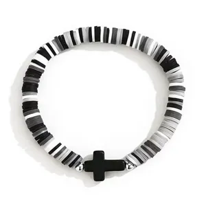 Gros plan sur l'élégant bracelet élastique en perles heishi noir et blanc avec croix.