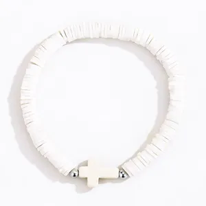 Détail du bracelet de perles heishi blanches avec pendentif croix style bohème chic.