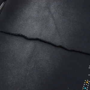 Detailed view of washed black casual shorts fabric featuring raw edge and colorful rhinestones.