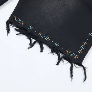 Close-up detail of black washed denim shorts hem with fringe and colorful rhinestone studs.