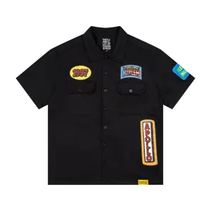 Close-up detail of black short-sleeve work shirt featuring embroidered colorful chest patches.