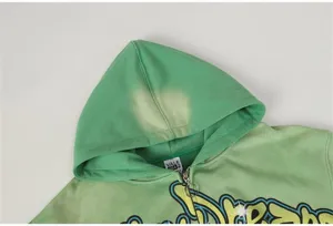 Green washed zip-up hoodie detail showcasing graffiti letter print and adjustable hood.