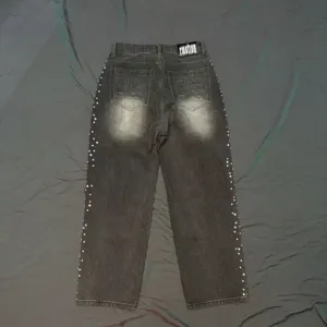 Detailed view of dark grey washed denim jeans featuring side rhinestones and gothic back pocket embroidery.