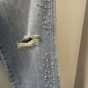 Close-up detail shot of light wash distressed denim jeans featuring rhinestone embellishments.