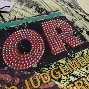 Detailed view of rhinestone letter graphic on washed streetwear t-shirt fabric texture.