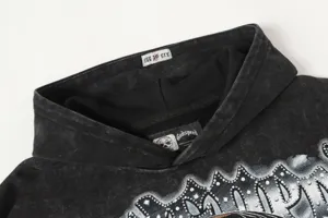 Detailed view of black washed streetwear hoodie collar with custom brand label and studs.