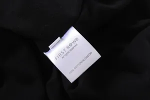 Close-up detail shot of the brand label and 100% cotton material inside a black t-shirt.