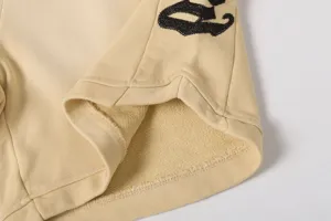 Vista dettagliata di pantaloncini casual in cotone beige con orlo a costine e ricamo nero.