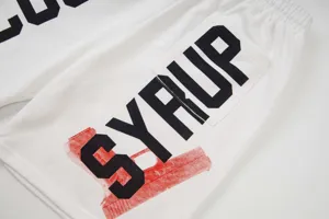 Dettaglio pantaloncini casual bianchi, stampa con lettere SYRUP nere e design grafico rosso.