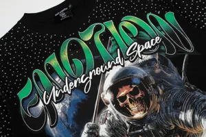 Vista detallada de camiseta streetwear negra con pedrería, estampado de calavera y letras degradadas.