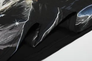Primer plano del dobladillo de camiseta negra de manga corta con estampado de galaxia y costuras.