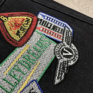 Λεπτομερές κοντινό πλάνο από κομψά κεντημένα μπαλώματα και πολύχρωμα σήματα σε μαύρο τζιν ύφασμα.