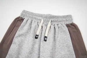 Close-up of gray sweatpants drawstring waist with brown side panels and logo tips detail