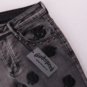 Close-up detail shot of washed grey denim shorts featuring gothic embroidery and rivet accents.