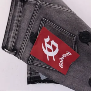 Close up detail of washed black denim shorts featuring red label and gothic embroidery.