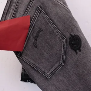 Close-up detail of grey denim shorts featuring black embroidery on the pocket and stylish logo.