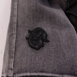 Detailed view of grey denim shorts featuring black embroidered logo, premium street style fashion.