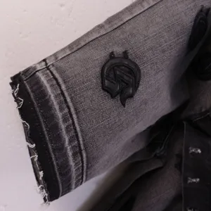 Close up of distressed black denim shorts cuff with gothic embroidery detail and frayed edge.
