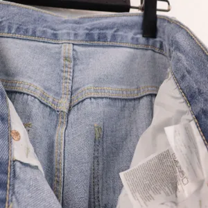 Denim jeans detail view featuring washed blue fabric, yellow stitching and inner wash label.