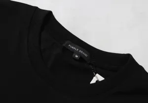 Close-up detail shot of the black t-shirt collar featuring brand logo tag and size M label.