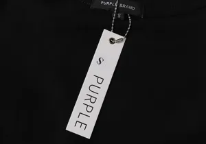 Close-up detail of the black t-shirt collar label and hanging tag with purple letters.