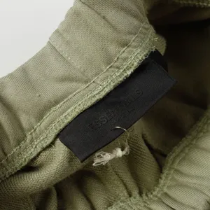 Detail shot of the green sweatpants waistband with black ESSENTIALS brand logo label.