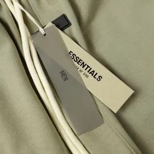 Detail view of ESSENTIALS high street sweatpants, showing green fabric, drawstrings, and brand tags.