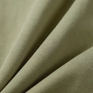 Close-up detail shot of soft sage green cotton blend knit fabric with natural folds and fine texture.