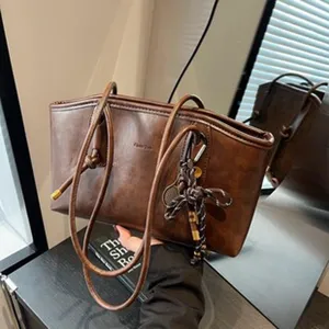 Nahaufnahme der braunen PU-Leder-Schultertasche mit schmalen Trägern und schickem Web-Anhänger.