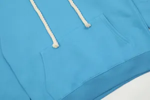 Primo piano dettaglio di felpa con cappuccio blu con coulisse bianche spesse e tasca a marsupio.