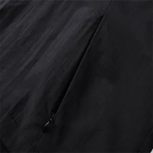 Close-up detail of black jacket fabric with zipper pocket, showing fine stitching texture.