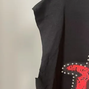 Λεπτομέρεια μαύρου αμάνικου τοπ με κόκκινο τύπωμα και λαμπερά στρας υψηλής αισθητικής.