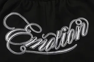Detailed close-up shot of black streetwear shorts featuring white cursive embroidery text Emotion.