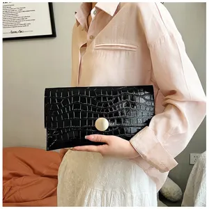 Sac pochette enveloppe noir gaufré croco avec fermoir métallique rond doré en gros plan