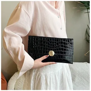 Détail de pochette noire motif crocodile, design minimaliste élégant avec bouton doré.