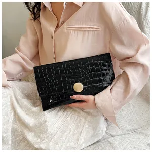 Gros plan de la pochette enveloppe en cuir verni noir motif crocodile avec fermoir rond doré.