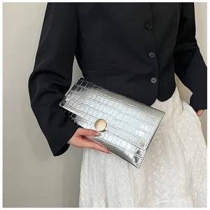 Sac clutch enveloppe en motif crocodile métallisé argenté avec fermoir rond doré.