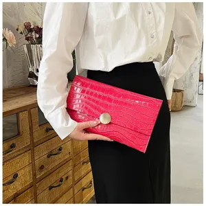 Gros plan sur la pochette enveloppe rose motif crocodile avec fermoir rond doré.
