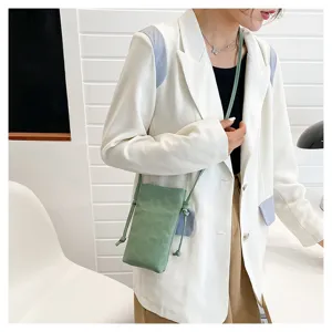 Gros plan détaillé du sac bandoulière téléphone vert clair élégant porté par le modèle.