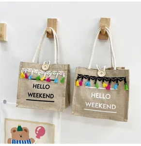 Gros plan de detail sur le sac cabas en lin avec pompons colores et bouton en bois.