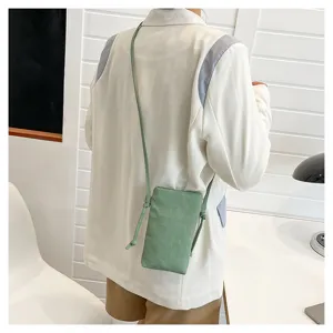 Vue détaillée d'un petit sac bandoulière de téléphone vert minimaliste porté en intérieur.
