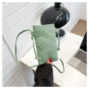 Vue détaillée d'un sac de téléphone bandoulière en toile verte avec sangle fine sur le bureau.