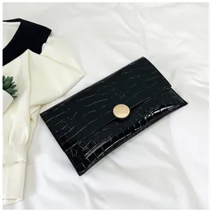 Détail de pochette noire motif croco, design minimaliste de sac enveloppe avec fermoir doré.