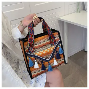 Primo piano della borsa a mano intrecciata etnica con cinghie geometriche colorate e nappe delicate.