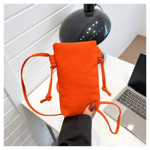 Vue détaillée du mini sac bandoulière de téléphone en toile orange avec fines bretelles sur le bureau.