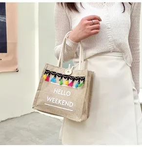 Vue détaillée d'un petit sac cabas en jute avec des glands colorés et l'inscription hello.