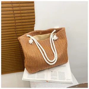 Nahaufnahme der geflochtenen Strohtasche mit weißen Seilgriffen und Quasten für den Sommer.